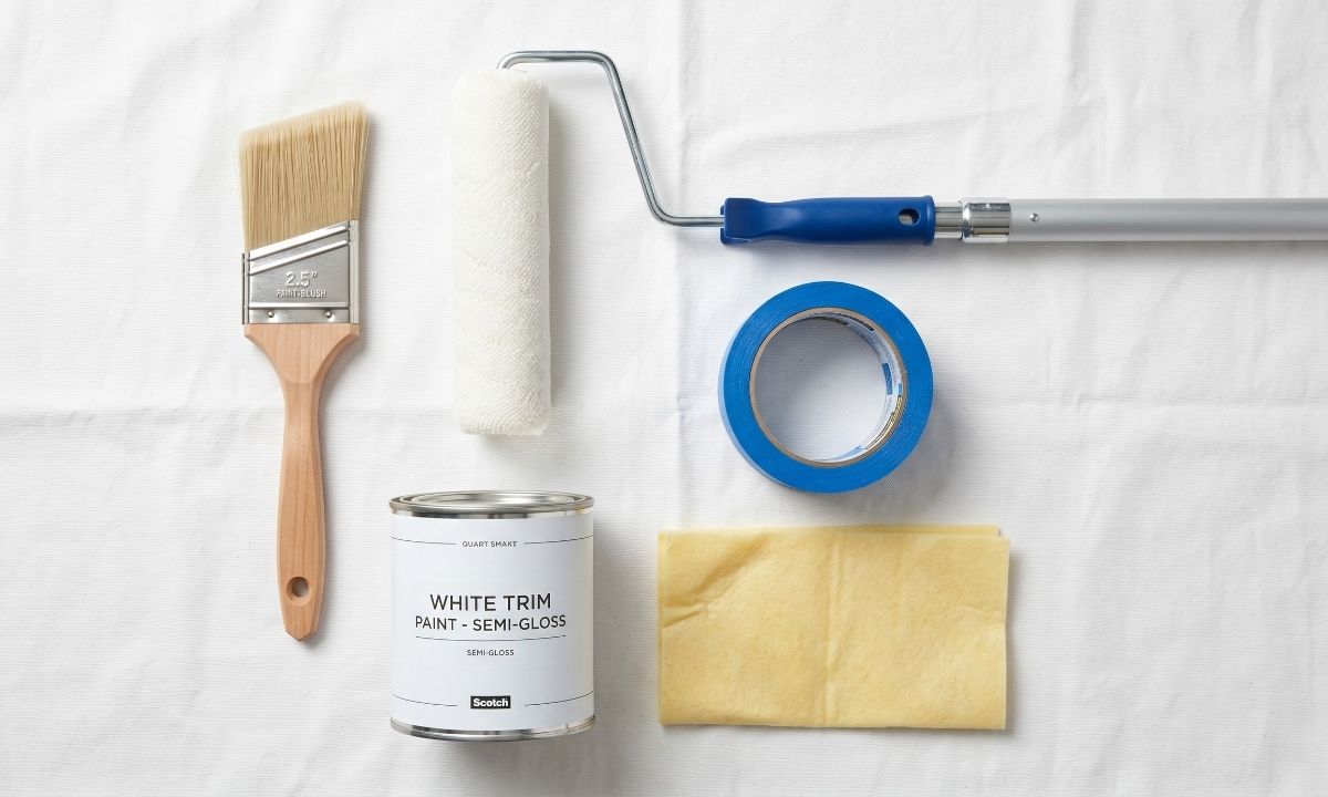 Essential tools for painting ceilings and trim including sash brush, roller, and painter's tape laid flat