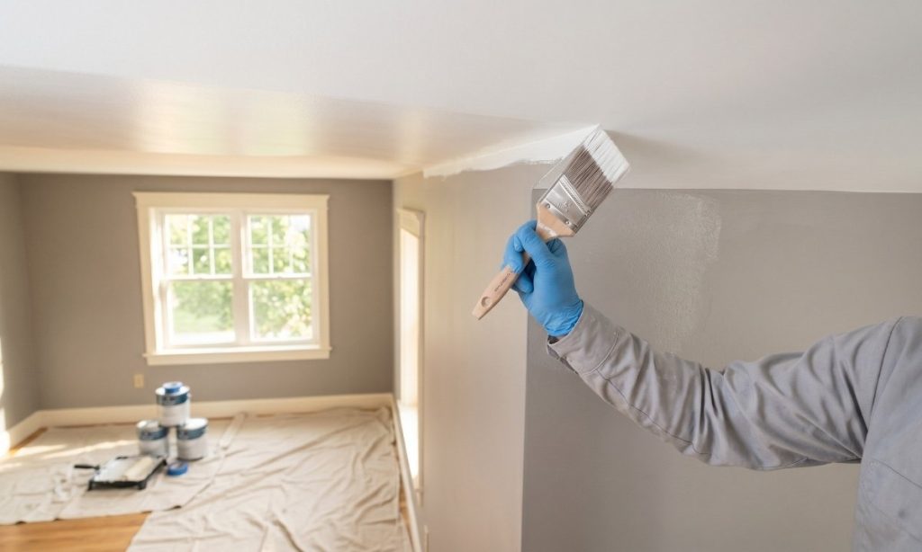 Painter cutting in a clean line between white ceiling and grey wall with an angled sash brush