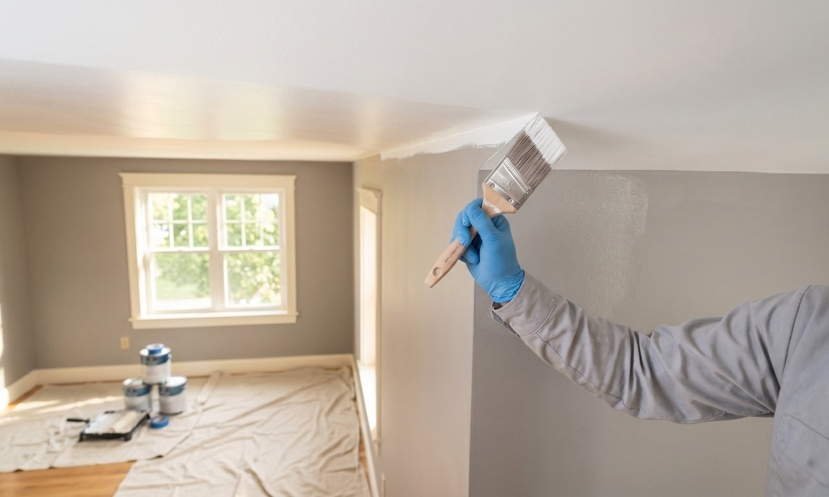 Painter cutting in a clean line between white ceiling and grey wall with an angled sash brush